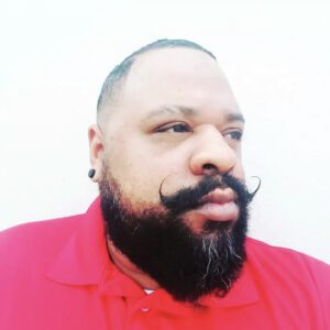 A man with a beard and mustache wearing a red shirt.